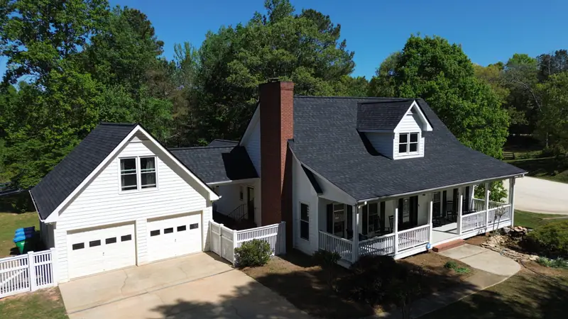 After: new charcoal architectural shingle roof on a white farmhouse with a wraparound porch